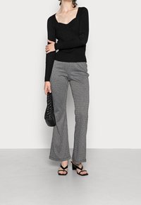 Svart ribbad långärmad topp i kombination med rutiga utsvängda byxor. Modellen håller en svart vävd handväska och har på sig svarta sandaler med remmar.