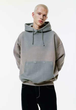 Overdimensioneret hættetrøje i gradient grå stof, med en front kangaroo-lomme med distressed detaljer. Kombineret med mørke jeans.