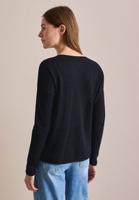 Mörkblå långärmad tröja med en strukturerad stickad design, med en bred halsringning och avslappnad passform, bärs över ljusblå jeans.
