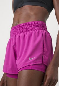 Růžové Nike šortky s elastickým pasem, postranními rozparky a malým stříbrným logem v dolním levém rohu. Vyrobené z lehkého, hladkého materiálu.
