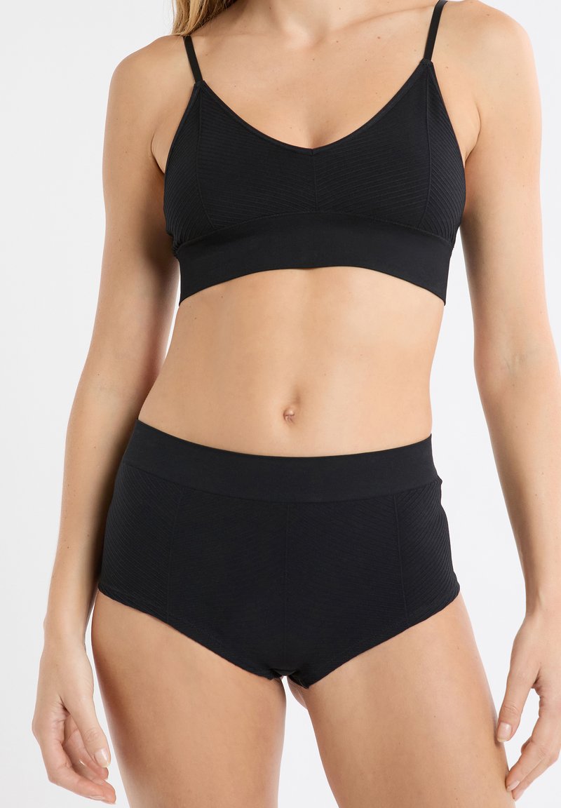 Top reggiseno nero con spalline sottili, caratterizzato da una texture a costine e una fascia liscia. Abbinato a slip a vita alta neri con una texture simile.