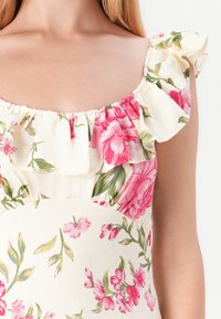 Blommig klänning med volangband, prydd av rosa och gröna blommor på en krämfärgad bakgrund. Mjuk tyg och figursydd överdel.