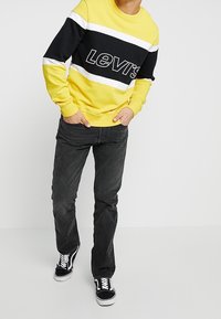 Žlutá a černá pruhovaná mikina s bílými akcenty, s logem Levi's. V kombinaci s tmavě šedými džíny a černými teniskami.