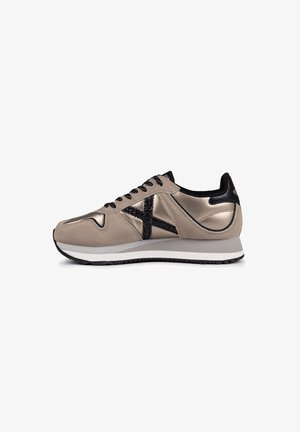 Zapatos deportivos con parte superior de ante beige y metálico, con un acento texturizado negro y cordones, medios sueles blancas y suela de goma negra.