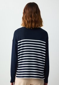 Granatowy sweter w białe paski z jednolitym granatowym tyłem. Posiada długie rękawy i luźny krój, wykonany z miękkiego materiału dzianinowego.
