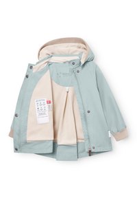 Svetlo modra otroška jakna z bež flis podlogo, kapuco, zadrgo, pritisnimi gumbi in etiketo za navodila za nego znotraj.