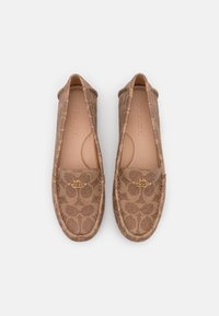 Des chaussures à enfiler brunes à motifs, fabriquées à partir d'un matériau texturé, avec un accent logo doré à l'avant et des coutures le long des bords.