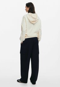 Cream hoodie with a large back pocket and drawstring hood, paired with loose-fitting navy cargo pants featuring side pockets and flaps.