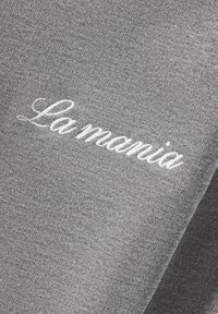 Hall halli dressipluuskangas sileda tekstuuriga, millel on valge tikandiga kiri "La mania" kursiivkirjas.