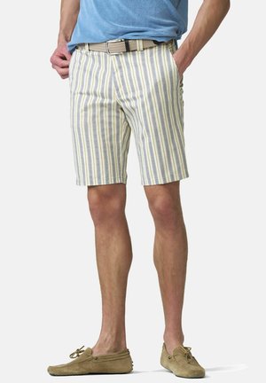 Man die beige, grijs en wit gestreepte korte broek met verticale strepen draagt, met een gevlochten riem en beige suède loafers, handen in de zakken, staand.