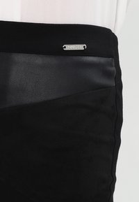 Černá sukně s hladkým koženým pasem a zamatovým tělem s prošívanými akcenty, ukazující strukturovaný, vícevrstvý design.