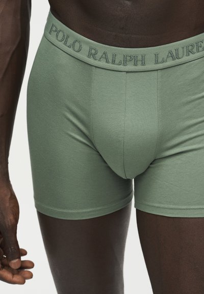 Αρσενικός κορμός με πράσινα boxer Polo Ralph Lauren, με ορατό το όνομα της μάρκας στη μέση, σε απλό φόντο.