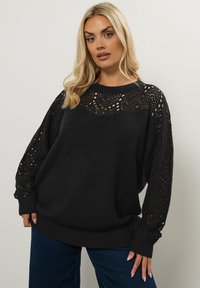 Svart oversized tröja med en texturerad kropp och en virkad mönstrad ok och ärmar. Långa ärmar med ribbade manschetter.