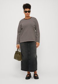 Top de manga larga a rayas en marrón y blanco, combinado con una falda de mezclilla negra de tiro alto. Los accesorios incluyen un bolso verde oscuro y zapatos negros.