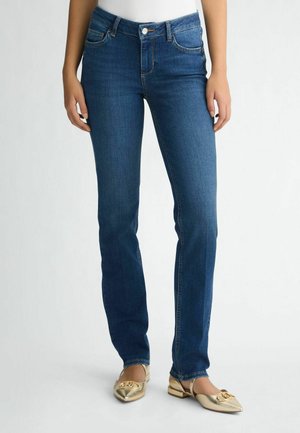 Tumedat sinised teksad slim-fit lõikega, viis taskut ja nööbiga sulgemine. Kandmine koos kuldsete baleriinadega, millel on dekoratiivne paeladetail.