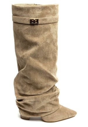 Botte beige en daim souple et ample, avec un bout pointu et une lanière à boucle rectangulaire dorée près du haut.