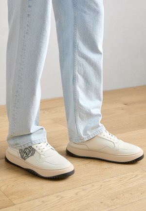 Baltas ādas sporta apavi ar teksturētu melnu lauva dizainu sānos, ar noapaļotu purngalu un mīkstu beigu zoli.