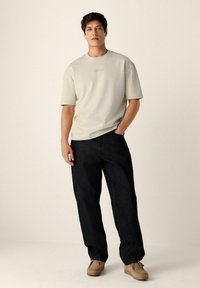Camiseta de manga corta gris claro con un acabado texturizado, combinada con pantalones vaqueros oscuros y holgados y zapatos de ante color tostado. Diseño simple, sin patrones visibles.