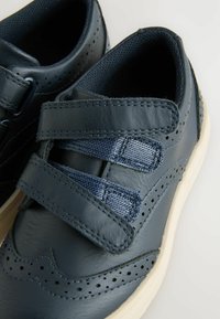 Granatowe skórzane buty z dwiema fabricznymi zapięciami na rzep, perforowanymi detalami i białą gumową podeszwą. Teksturowane wnętrze.