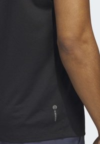 Camiseta deportiva negra con una superficie texturizada, que presenta un pequeño logo "AEROREADY" en el dobladillo. Se ve un primer plano de un brazo.
