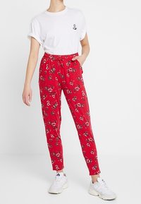 Röda blommönstrade byxor med elastisk midja, sidofickor och avsmalnande ben, tillsammans med en vit t-shirt med rund hals.