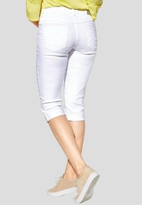 Witte capri-broeken met opgerolde pijpen, voorzien van twee achterzakken. Gecombineerd met lichtbeige sneakers. Eenvoudig ontwerp en gladde textuur.