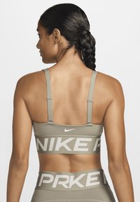 Oliven grønnidrettsbh med justerbare stropper og hvitt logo; har bredde med "NIKE" trykket i fet skrift. Glatt tekstur, atletisk design.