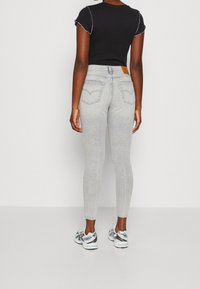 Vaqueros skinny de tiro alto, gris claro, con una textura suave, diseño de cinco bolsillos y un detalle de costura minimalista en los bolsillos.