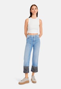 White cropped tank top, light blue wide-leg jeans with leopard print cuffs, and gray platform sneakers. Smooth texture, casual fit.