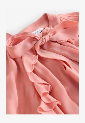 Blouse en chiffon rose avec un nœud noué au niveau du col, présentant des bords froncés et une texture douce, mettant en valeur un design en tissu fluide.