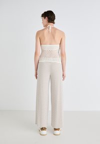 Gehaakte haltertop met open rug, gecombineerd met brede gestreepte broek in zacht beige en crèmewit. Sneakers maken de outfit compleet.