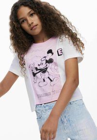 Hvid t-shirt med lyserødt gradient og Mickey Mouse-design, korte ærmer og rund halsudskæring. Lys blå jeans med falmet tekstur.