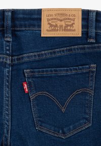 Tumesinised teksapüksid, mille vöökohal on nahast silt "Levi Strauss & Co." ja õmmeldud tagatasku V-kujuline muster.