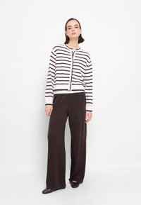 Cardigan a righe in bianco e marrone, con chiusura a bottoni, abbinato a pantaloni a gamba larga marroni scuri e ballerine marroni. Texture liscia e morbida.
