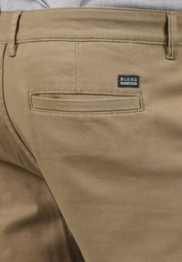 Chinos de mezcla de algodón en color marrón claro con un bolsillo trasero, que presenta una pequeña etiqueta negra "BLEND" encima. Textura suave y corte entallado.