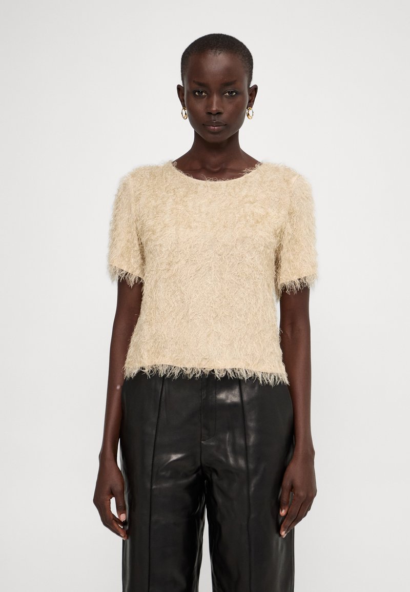 Top beige a maniche corte e pelose con scollatura rotonda, caratterizzato da un tessuto testurizzato. Abbinato a pantaloni in pelle neri.