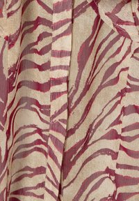 Tessuto a motivo con sfondo beige e strisce astratte di zebra rosse. Superficie leggermente strutturata con un design fluido.