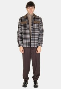 Camicia di flanella a scacchi in grigio, nero e bianco con accenti marroni, due tasche sul petto, abbinata a pantaloni marroni e scarpe nere.