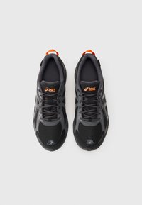 Um par de sapatilhas de corrida Asics, em preto e cinza, com logótipo laranja e puxador no calcanhar, vistas de cima sobre um fundo branco.