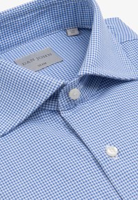 Primo piano di una camicia aderente a fantasia pied de poule blu e bianca con bottoni bianchi e colletto a punta piegato.