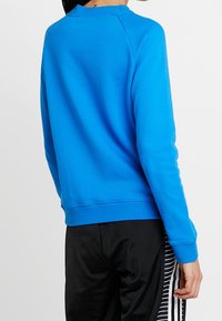 Světlá modrá mikina s kulatým výstřihem a raglánovými rukávy. Měkká textura látky s žebrovanými manžetami a spodním lemem. Černé kalhoty s pruhy.