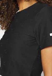 Femme portant un crop top noir ajusté avec des logos Nike Air subtilement embossés et une petite étiquette blanche avec le logo sur la manche.