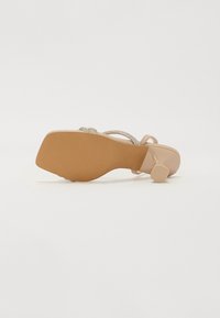 Sandalie con tacco alto color beige, con suola liscia, caratterizzate da fasce sottili decorate con strass argentati e un design con tacco a blocco.