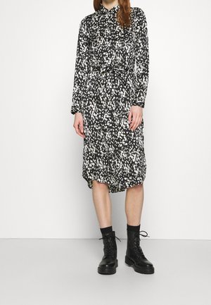 Czarna i biała sukienka z długim rękawem, o luźnym kroju, z paskiem w talii i wzorem w cętki, zestawiona z czarnymi, sznurowanymi butami typu combat.