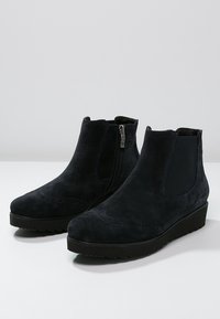 Par de botas de tobillo negras de ante con cremallera lateral y panel elástico, puntera redondeada y suela de goma con cuña baja.