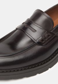 Mocassino in pelle marrone con finitura lucida, caratterizzato da una fascia superiore pronunciata e dettagli testurizzati, montato su una suola in gomma nera.