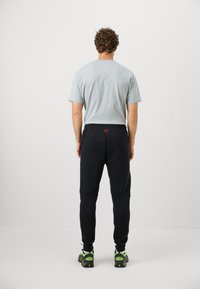 Grå kortærmet t-shirt kombineret med sorte sweatpants med et broderet rødt logo, elastisk talje og sorte sportssko med grønne accenter.