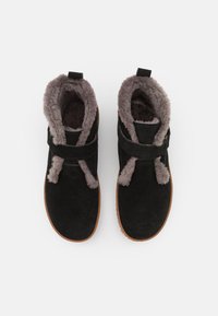 Black suede ankle boots with gray fur lining, a flat sole, and a strap across the front, featuring two fabric tassels for decoration.