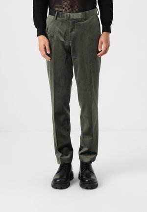 Olive green dress pants in a smooth fabric, featuring a straight cut, front pockets, and tailored fit, paired with black shoes.