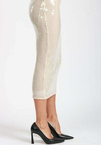 Gonna a tubino beige fino al ginocchio con texture in paillettes, tessuto a costine, orlo grezzo, abbinata a décolleté nere a punta.